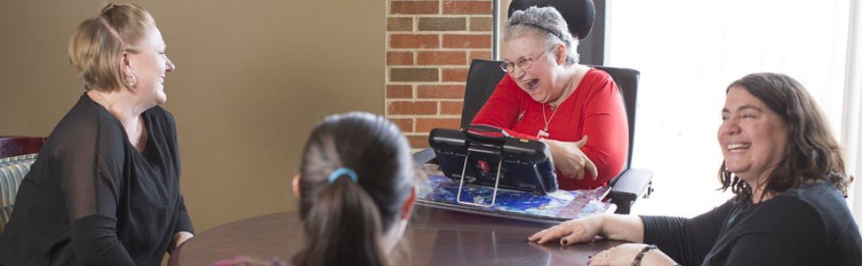 Woman laughing with friends while using an AAC device